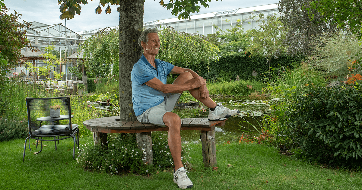 Foto van coach Cor van Ruijven van CvR VISIE op een bankje aan het water onder een boom.