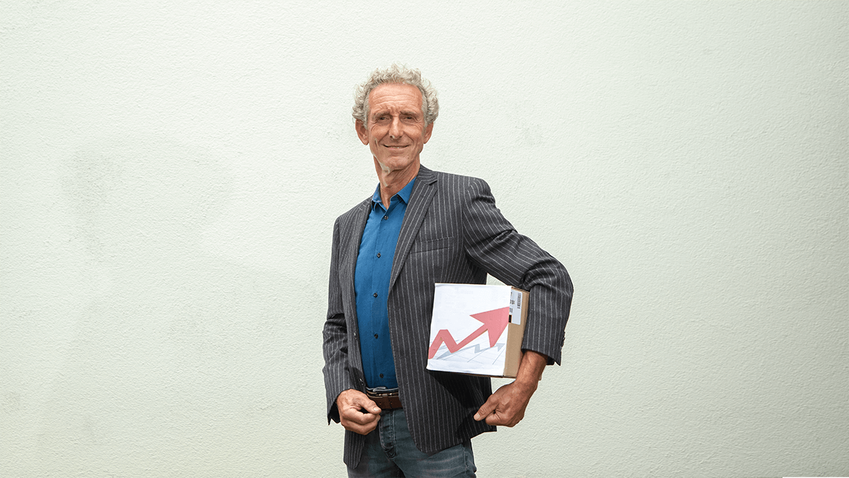 Foto van coach Cor van Ruijven van CvR VISIE. Op de foto draagt Cor een blauwe spijkerbroek en grijs gestreept colbert. Onder zijn arm draagt Cor van Ruijven een doos kopieerpapier.