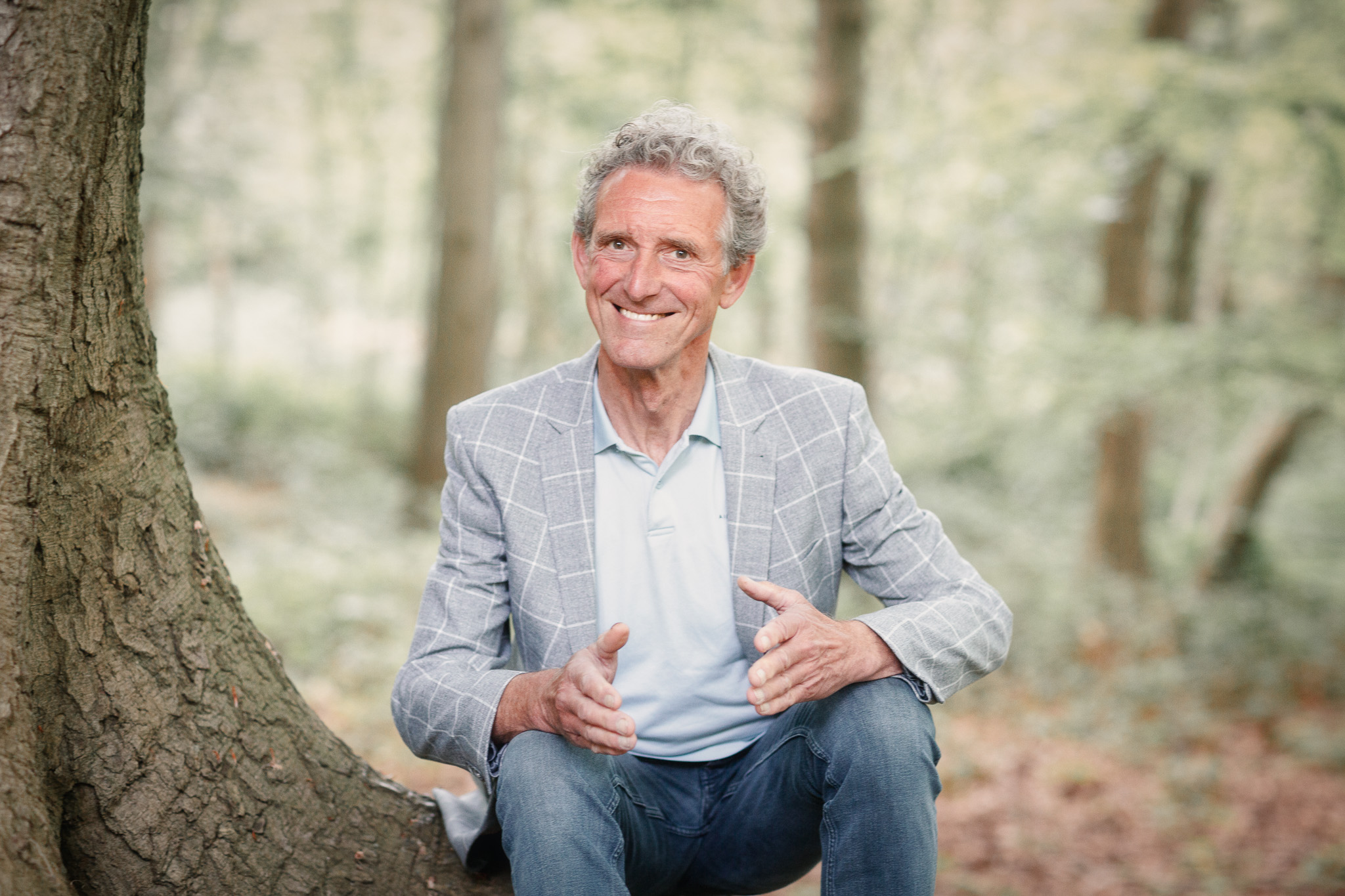 Cor van Ruijven zit in het bos op een boomstronk en is uitleg aan het geven aan de lezer.